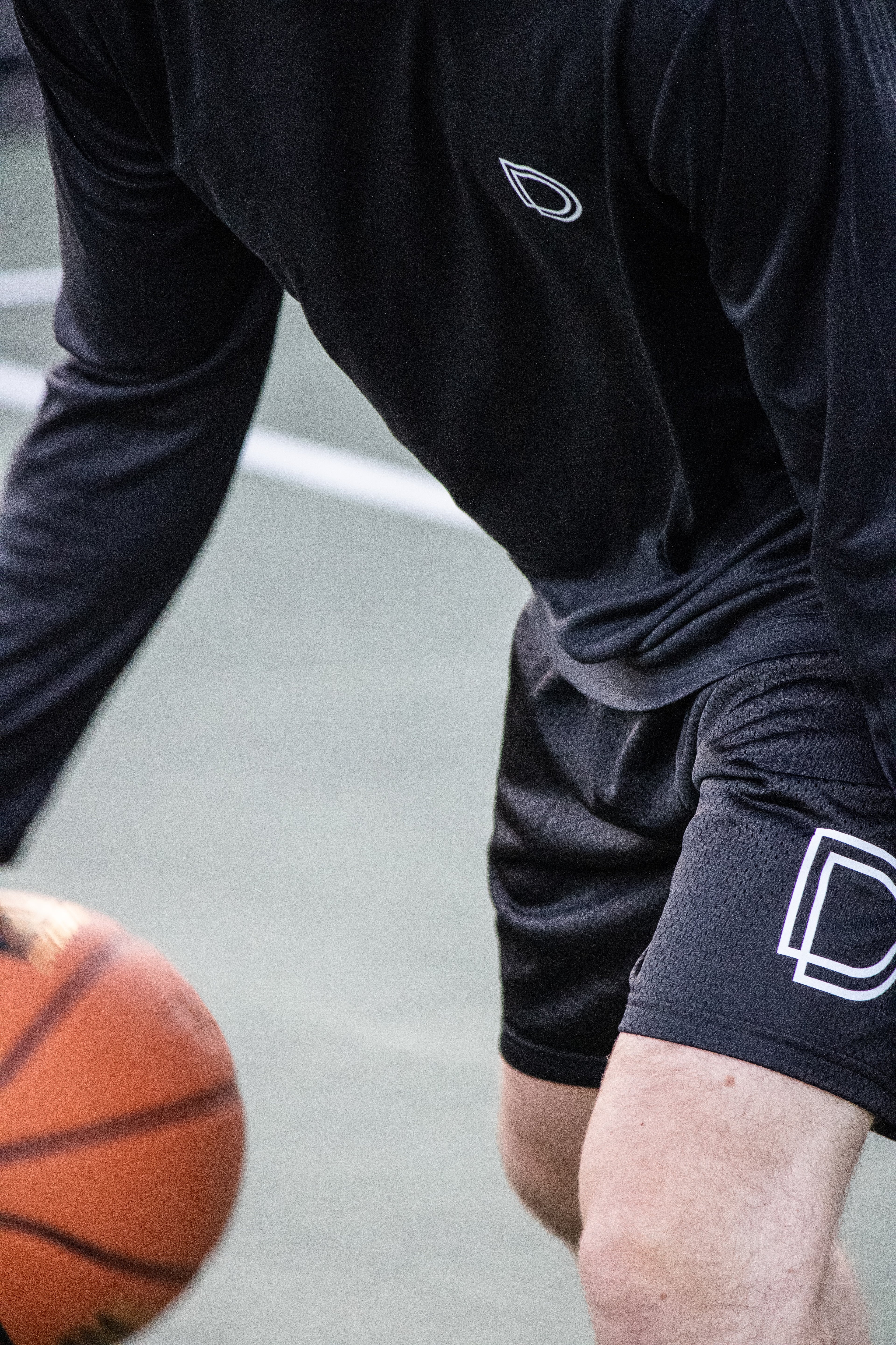 Person wearing black athletic shorts with a logo, holding a basketball on an outdoor court.